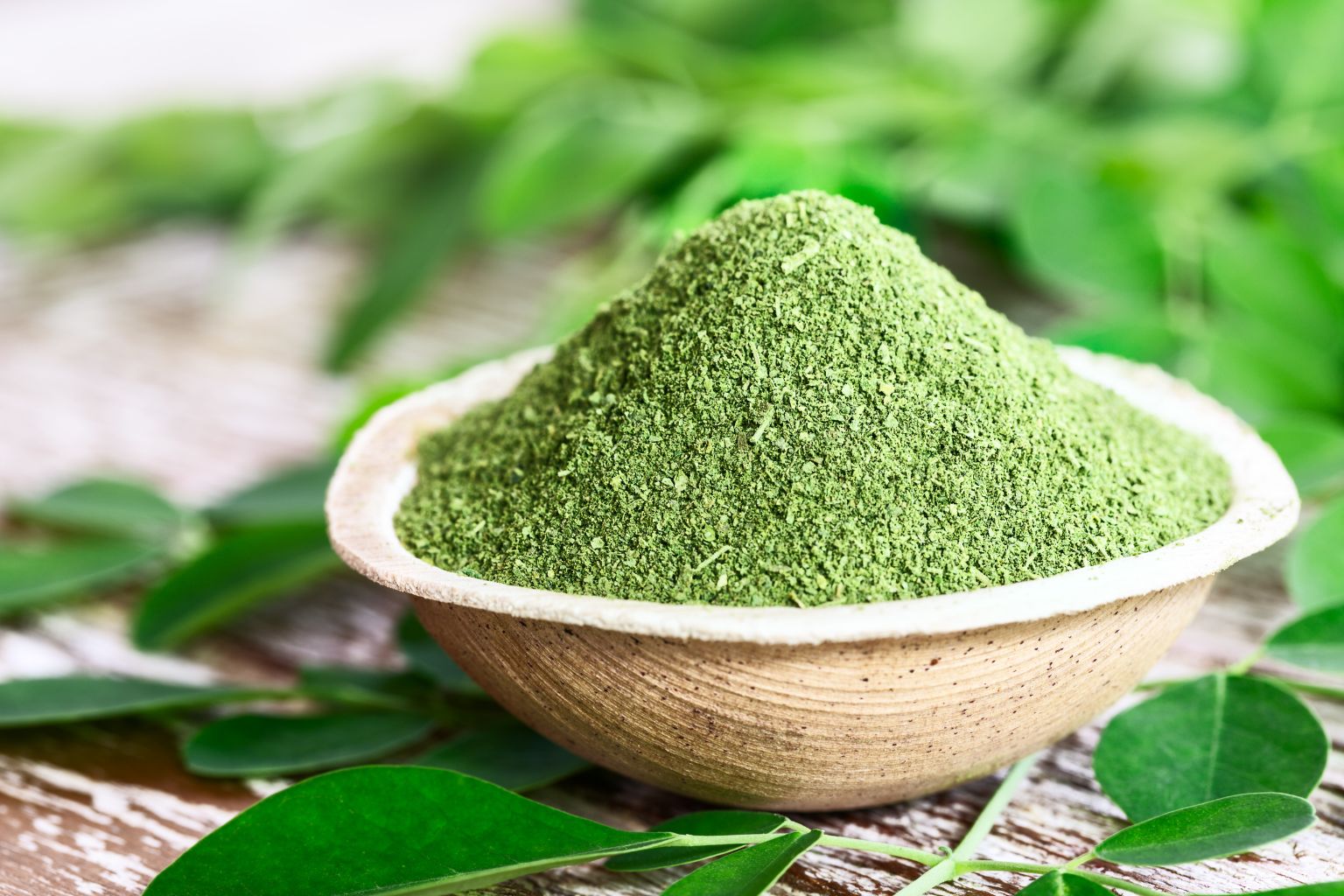 Bowl con polvo de moringa verde y cuchara de madera mostrando su uso nutricional