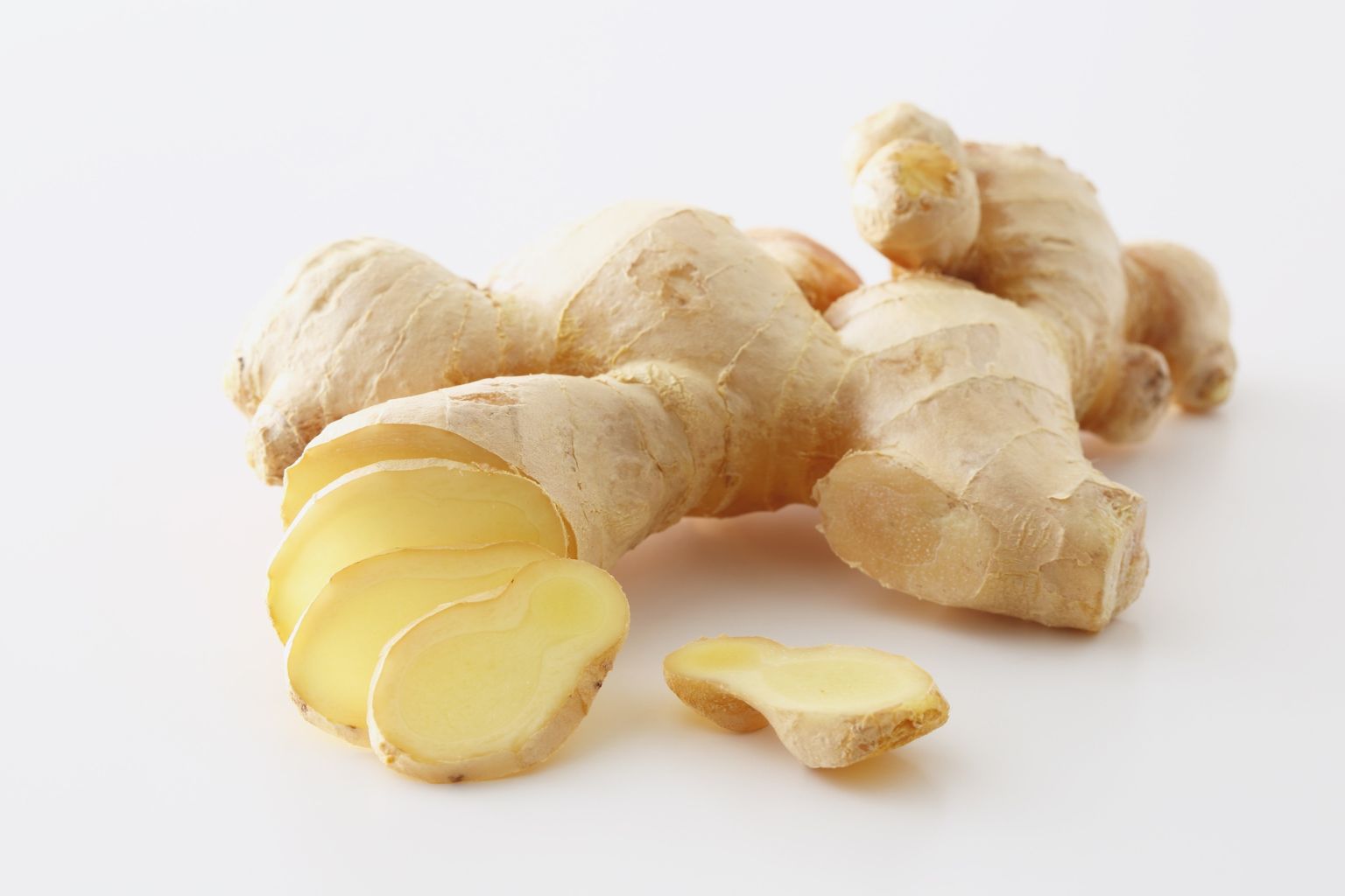 Raíz fresca de jengibre sobre superficie blanca con trozos cortados al lado